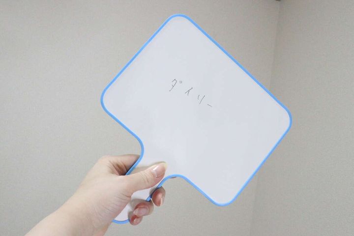 女性が「ダースリー」と書かれたホワイトボードを掲げる