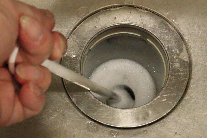 キッチンの排水口の中で排水管ブラシを動かし泡立てて掃除している