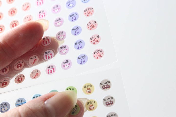 指で推し活柄のスケジュールシールを台紙から剥がそうとしている様子