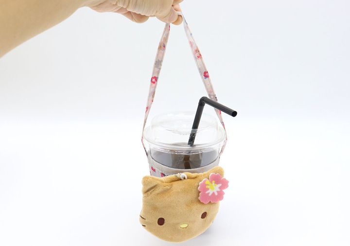 手で持ち上げられた、日焼けハローキティのカップスリーブにセットされたアイスコーヒー
