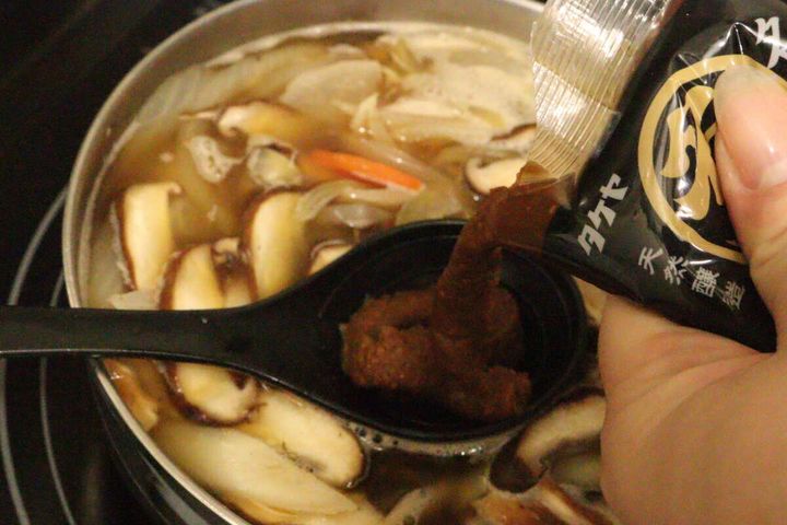 豚汁の具材が入った鍋にタケヤ名人のみそをスプーンで入れている
