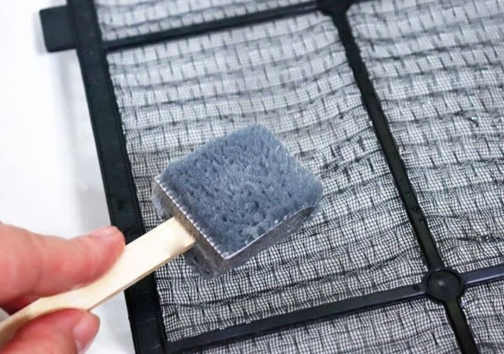 手でエアコンのフィルターメッシュスッキリ棒を使い、エアコンフィルターを掃除している様子