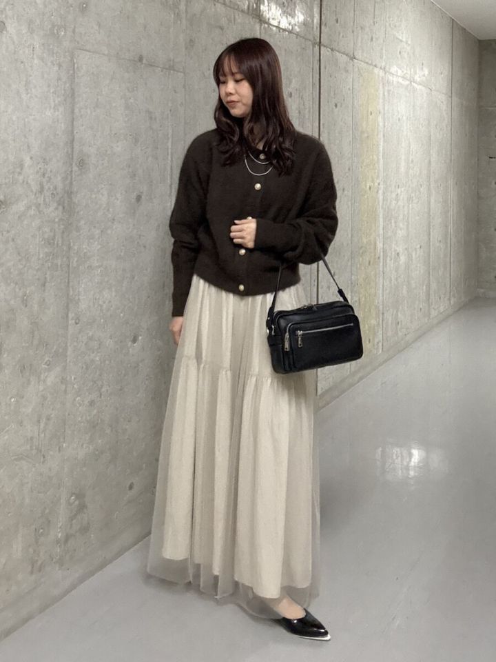 ヘアリーカーディガンとチュールスカートを着た女性が黒いバッグを持つ