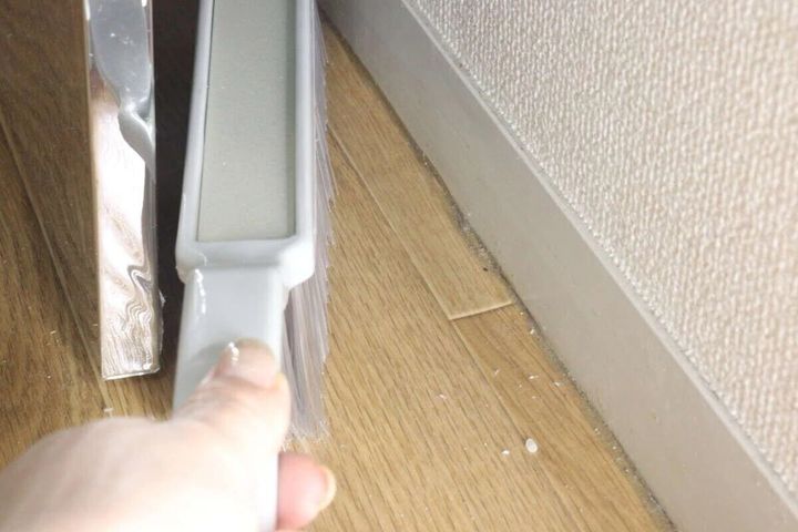 女性の手が「持ちやすいほうき」で壁と床の隙間のゴミをかき出している