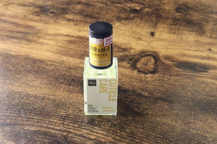 ダイソーの「キューティクルリムーバー」のボトルが木目調の台に置かれている