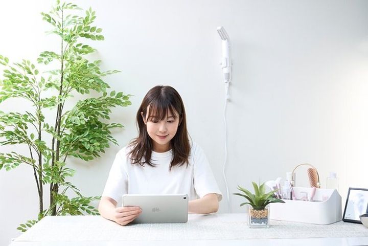 壁掛けドライヤーを背景に、タブレットを見る女性