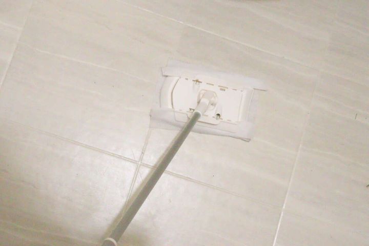 ダイソーのお掃除シートを装着したワイパーで、白いタイルの床を拭いている