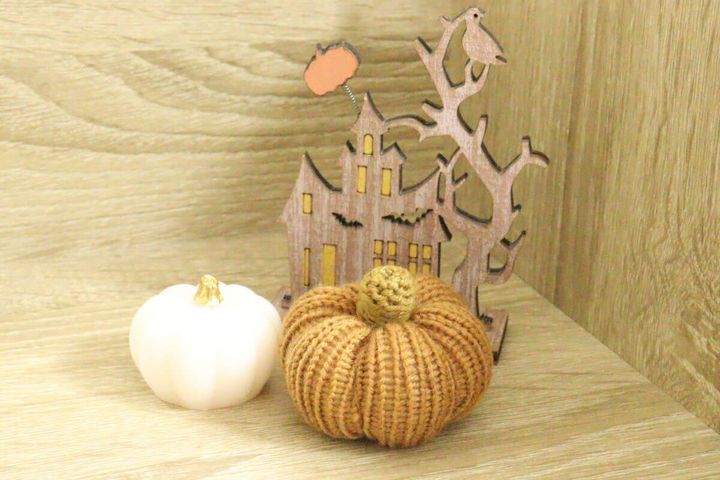 白いレジンと毛糸のかぼちゃが木製ハロウィン飾りと一緒に置かれている