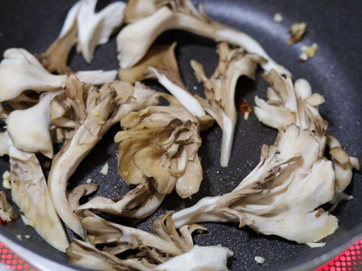 フライパンでまいたけと赤唐辛子を加えて炒めている様子