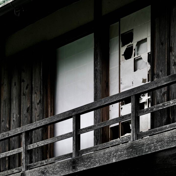 古びた木造建物の外観。木製の手すりの奥に、破れた障子が並んでいる。