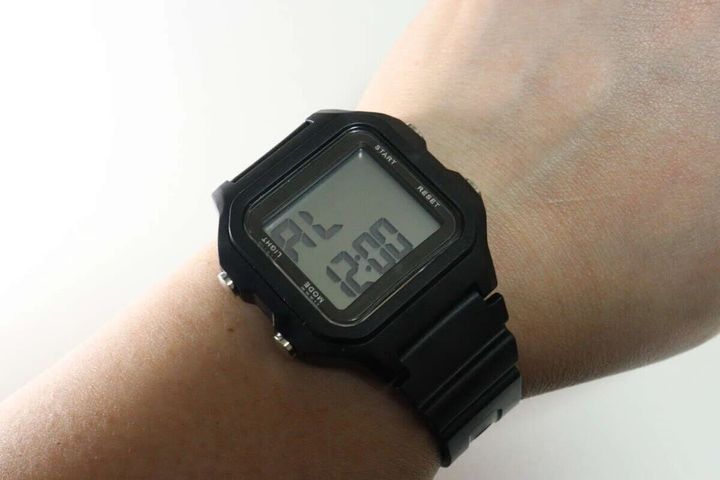 黒いスクエア型デジタルウォッチを腕に装着し、アラーム時刻を表示