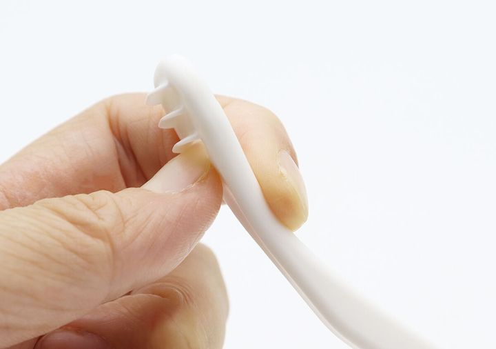 舌クリーナーの軸を指で曲げ、しなり具合を確認している