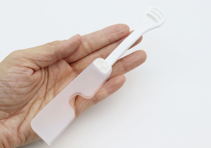 広げた状態の白い折りたたみ舌クリーナーを手のひらに乗せている