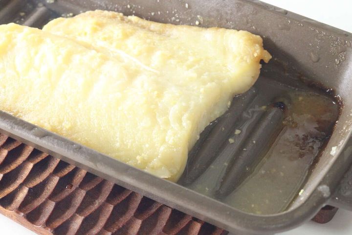 調理後の西京焼きと、トレーの底に溜まった余分な水分や油分のアップ