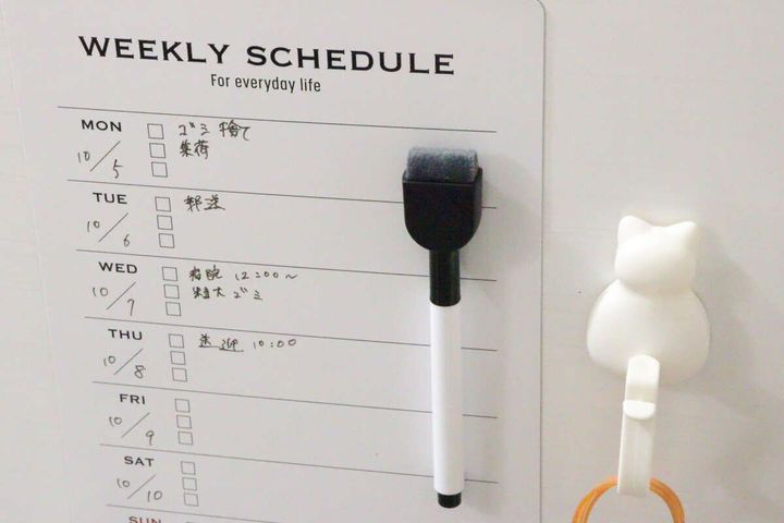壁に貼られた週間予定表とマーカー、白い猫のフック