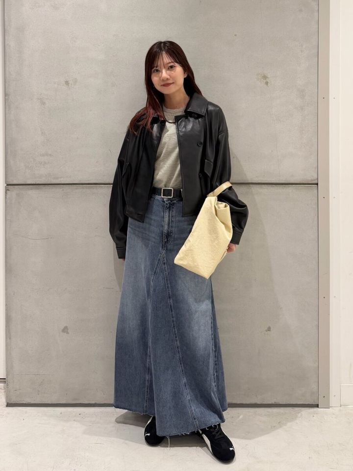 黒レザーブルゾンとフレアデニムスカートを着た女性が立つ
