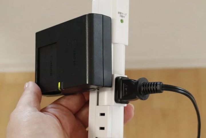 白い回転式電源タップに黒い大きな充電器と黒いプラグが挿さっている