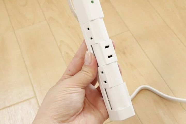 白い四角い電源タップの裏側にあるコンセントプラグを女性の手が持っている