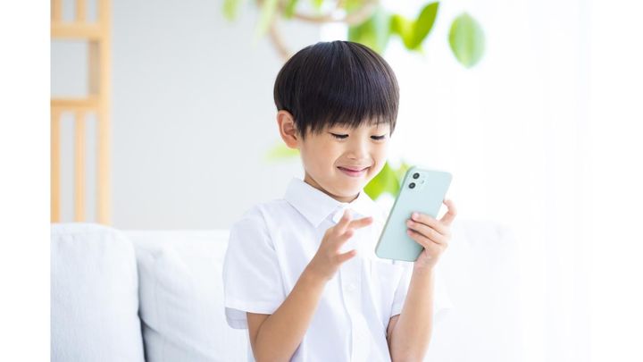 ソファでスマートフォンを笑顔で操作する男の子