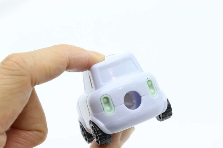右手で車型鉛筆削りを持ち、後部の鉛筆穴を見せている