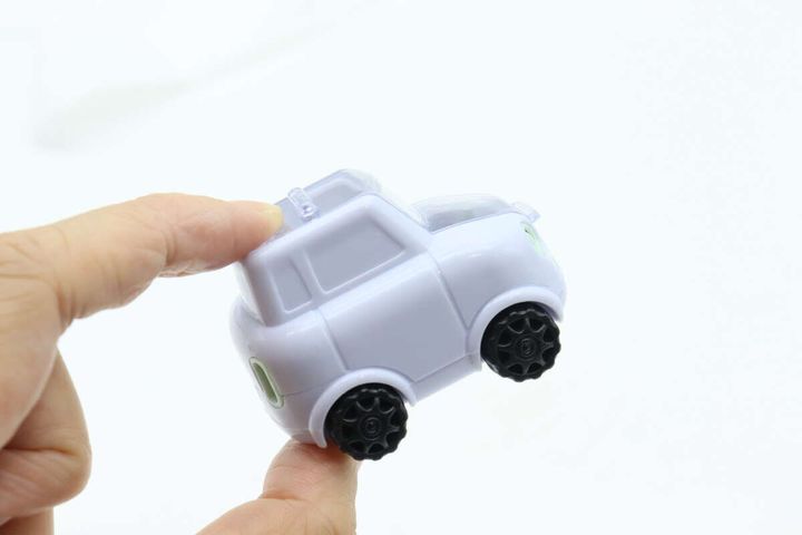 右手でパステルパープルの車型鉛筆削りを持ち上げている
