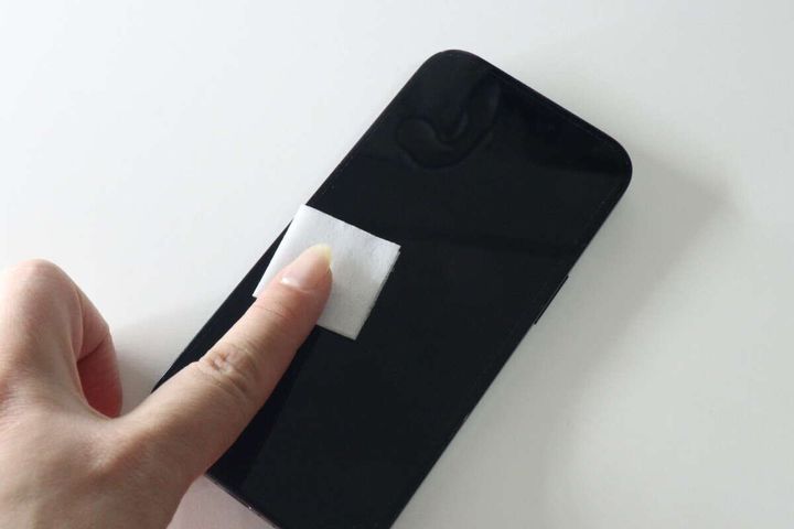 女性の手がスマホ画面をウェットシートで拭いている様子