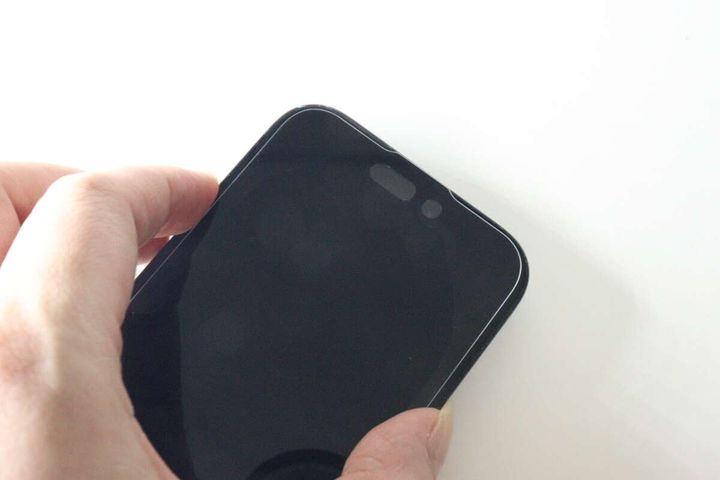 保護ガラスを貼り付けたiPhoneの画面上部を指で押さえている