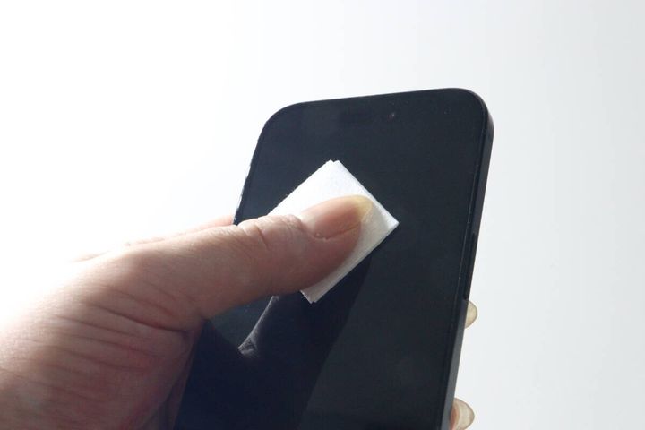 女性の手がスマホ画面の側面をウェットシートで拭いている様子