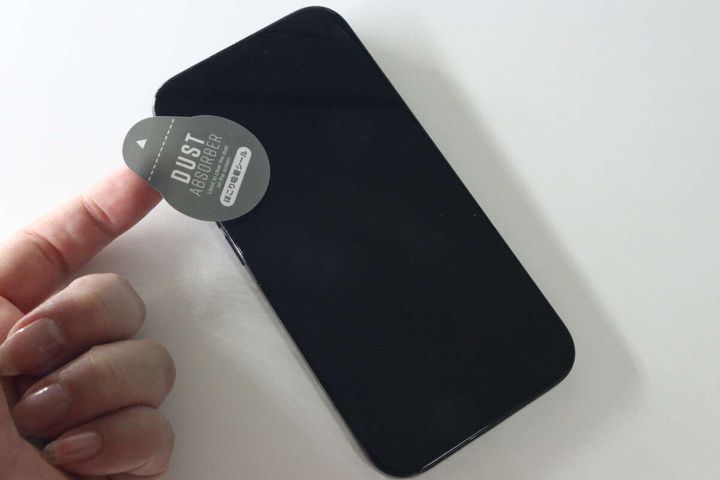 女性の手がホコリ取りシールでスマホ画面のホコリを取っている