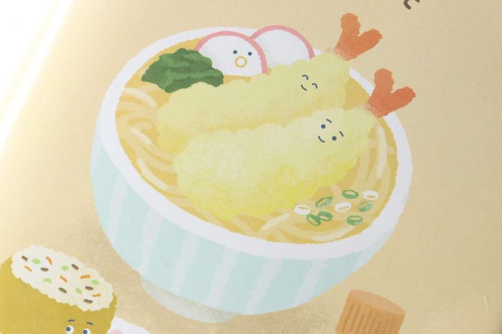 うどんの器に入ったエビ天とかまぼこのキャラクターのアップ