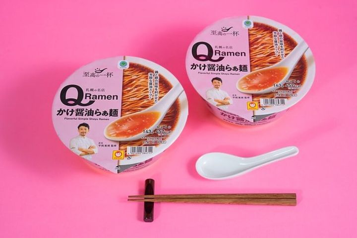 ピンクの背景に「QRamen かけ醤油らぁ麺」のカップ麺2つとレンゲ、箸が並ぶ