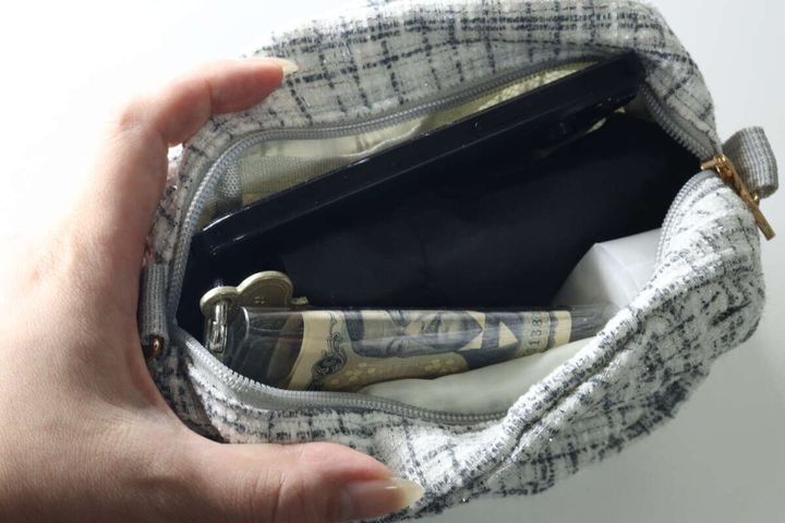 女性の手が、チェック柄のポーチに黒い折りたたみ傘を収納している様子