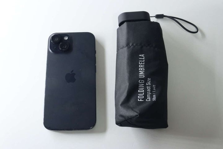 黒い折りたたみ傘とスマートフォンを並べ、コンパクトなサイズ感を比較している