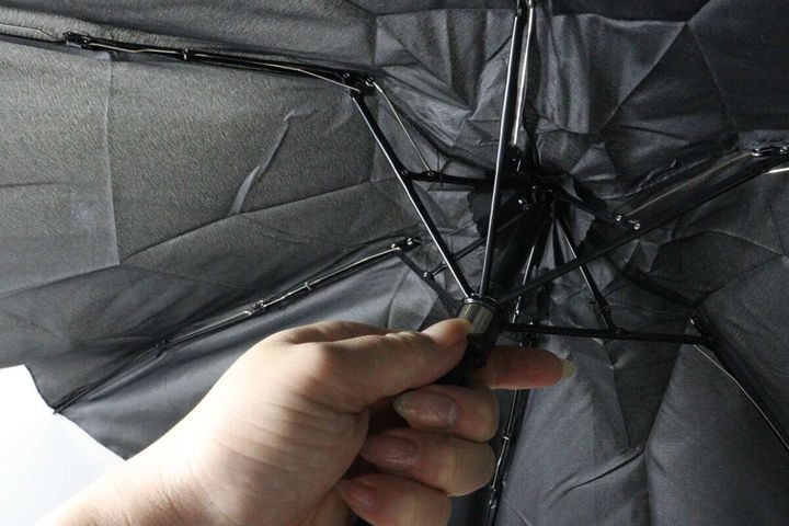 広げた黒い傘の骨組みと、傘の持ち手部分を握る女性の手のクローズアップ