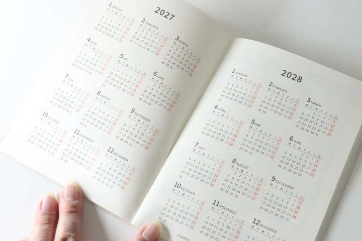 指で開かれた2027年と2028年の年間カレンダーページ