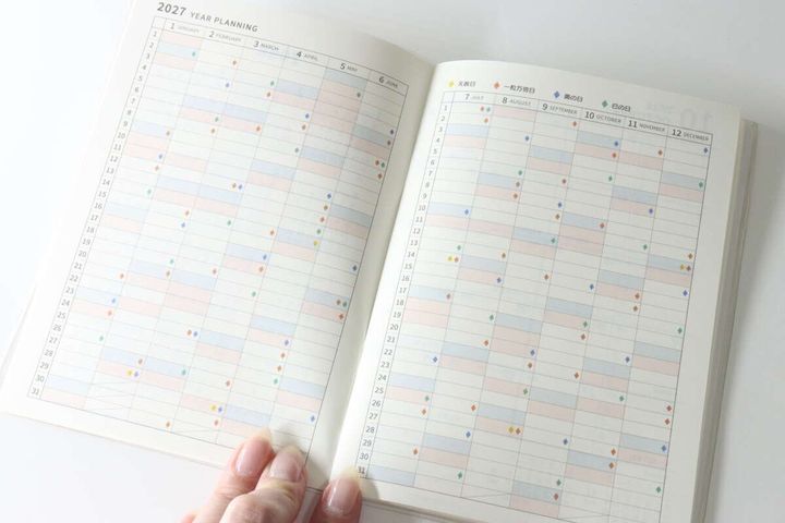 指で開かれた2027年の年間スケジュールページにカラフルな吉日マーク