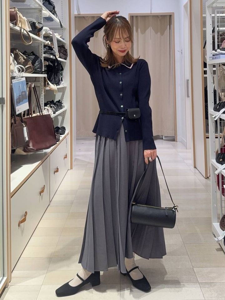 ネイビーのポロ襟カーディガンとプリーツスカートの女性