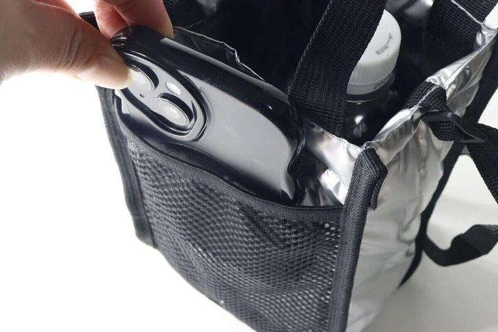 メッシュショルダーバッグのポケットに黒いスマートフォンを入れる手元