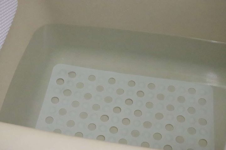浴槽の底に白い吸盤付浴槽マットが敷かれ、お湯が張られている