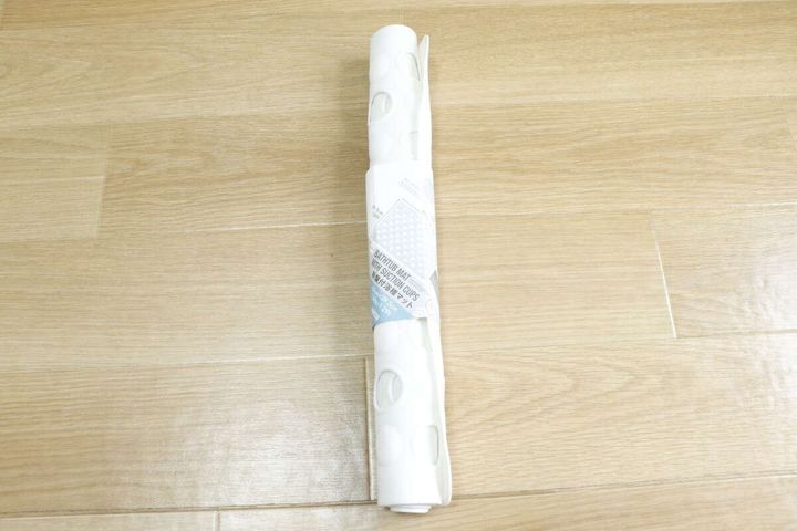 木目の床に置かれた、ロール状に巻かれた白い吸盤付浴槽マット