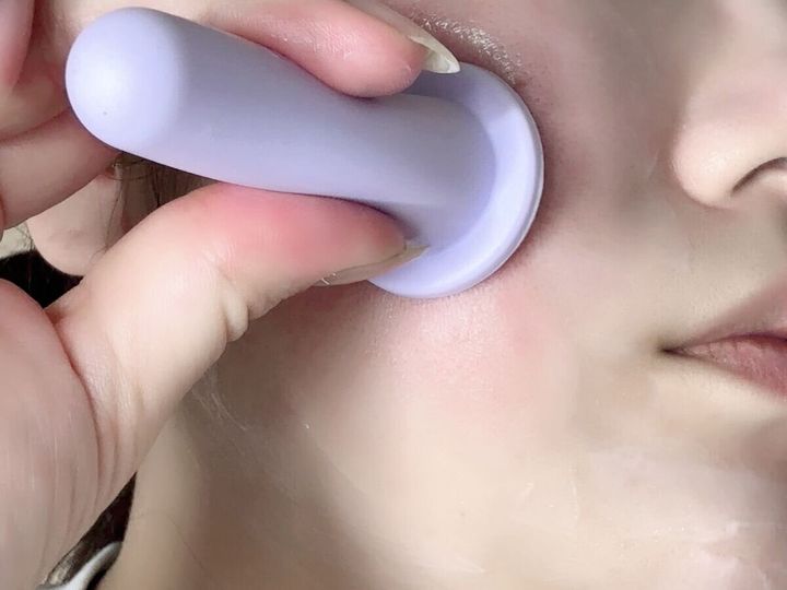 女性が顔の頬にラベンダー色のフェイシャルカッピングカップを吸着させている様子。