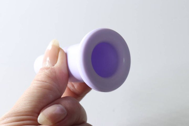 女性の指がラベンダー色のフェイシャルカッピングカップを持ち、吸い口部分が見える。