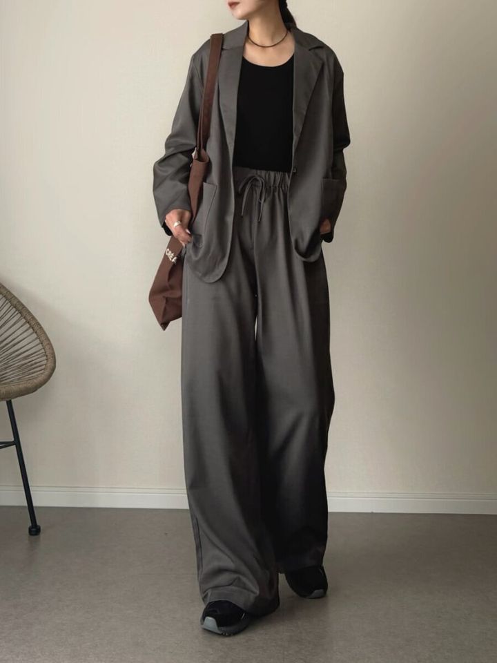 グレーのジャケットとワイドパンツを着て黒いインナーとスニーカーを合わせた女性