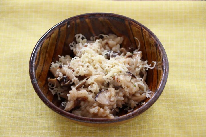 リゾット風にアレンジされたきのこピラフが木製の器に盛られチーズがかけられている