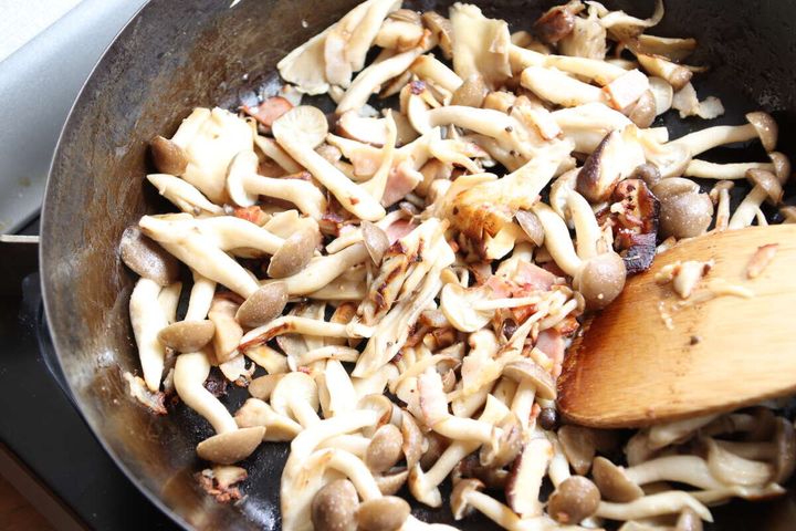フライパンでベーコンときのこを木べらで炒めている調理中の様子