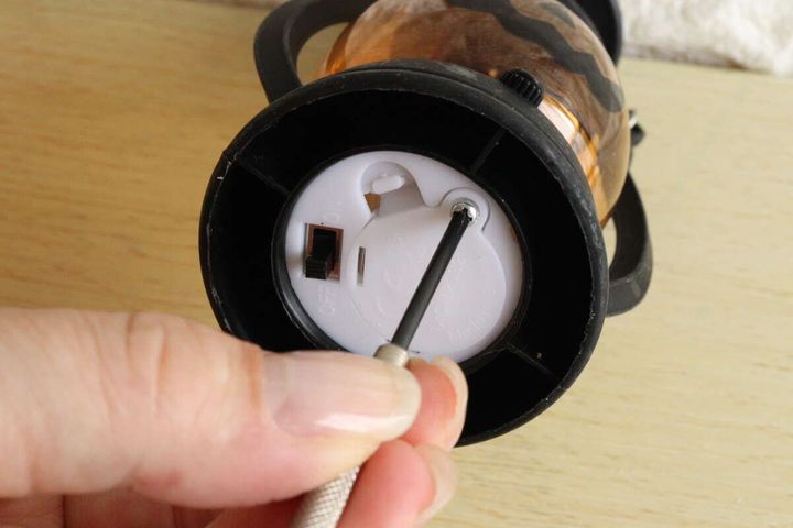 女性がLEDランタンの底面の電池蓋をドライバーで開けている