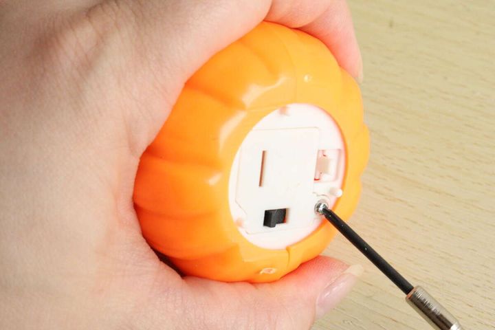 女性がパンプキンLEDライトの底面の電池蓋をドライバーで開けている