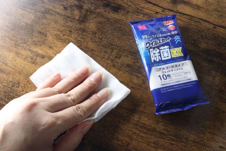 女性が除菌ウェットティッシュで木目のテーブルを拭いている