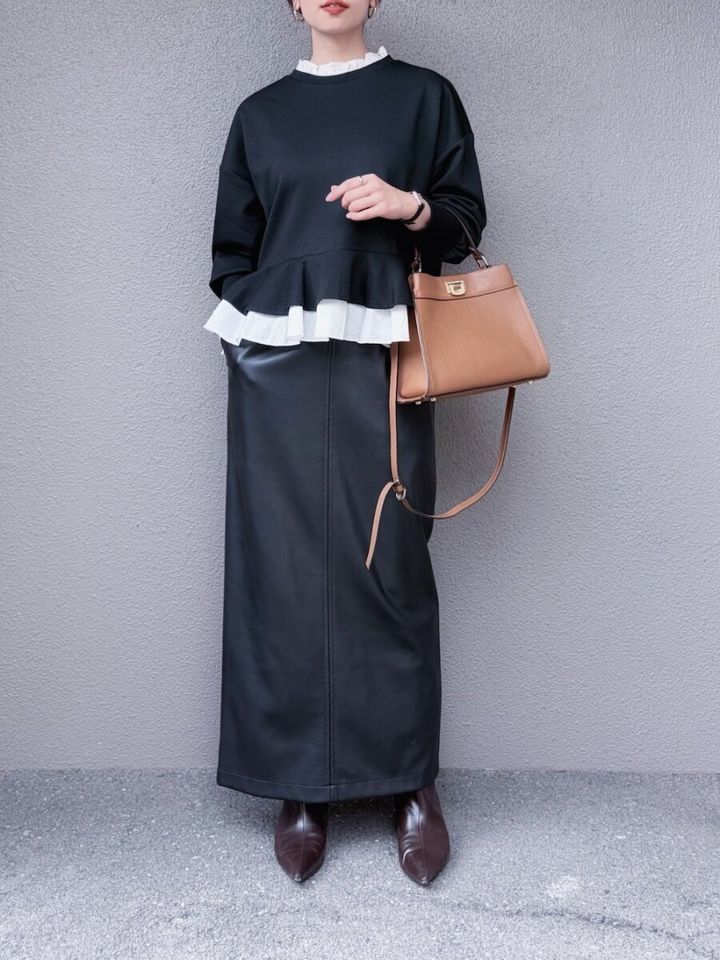 黒スウェットとレザーロングスカートの女性がバッグを持つ