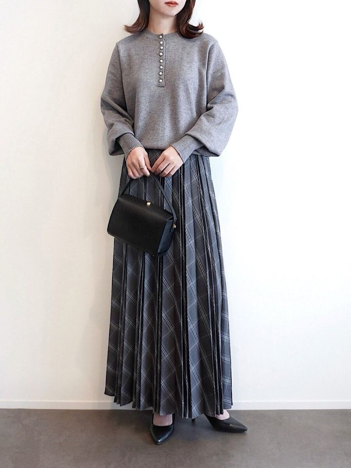 グレーのトップスとチェック柄プリーツスカートの女性